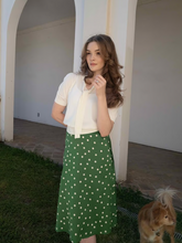 a lady wears a green polka dot skirt with a white blouse